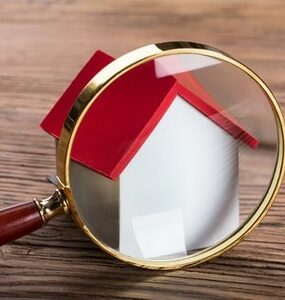 Magnifying glass in front of house representing home search or inspections