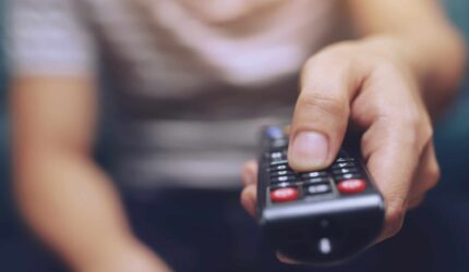 close up Television remote control in casual man hands pointing to tv set and turning it on or off. select channel watching tv on his sofa at home in the living room relax.