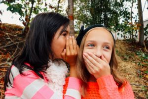 Two girls whisper secrets to each other