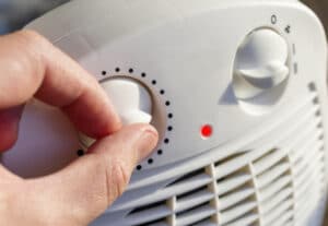 Man adjusts the temperature of the electric space heater at home.