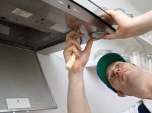 Repair man fixing exhaust hood in kitchen.