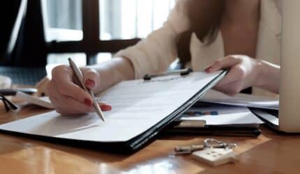 real estate agent assisting client to sign contract paper at desk with house model