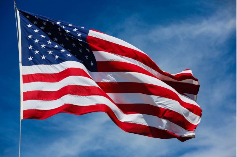 US flag flying on background of blue sky, white clouds